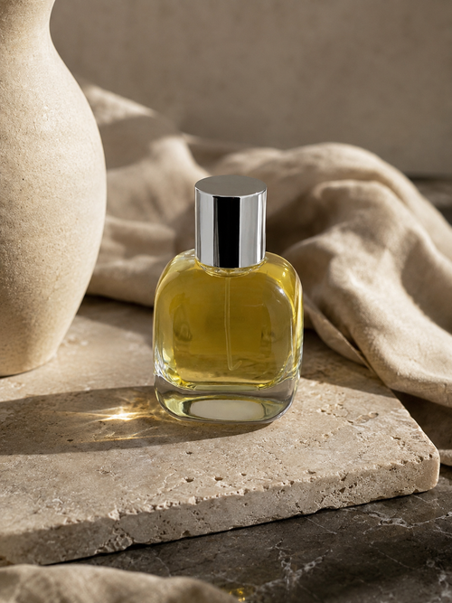 Amber Elixir eau de parfum bottle on travertine beside a stone vase
